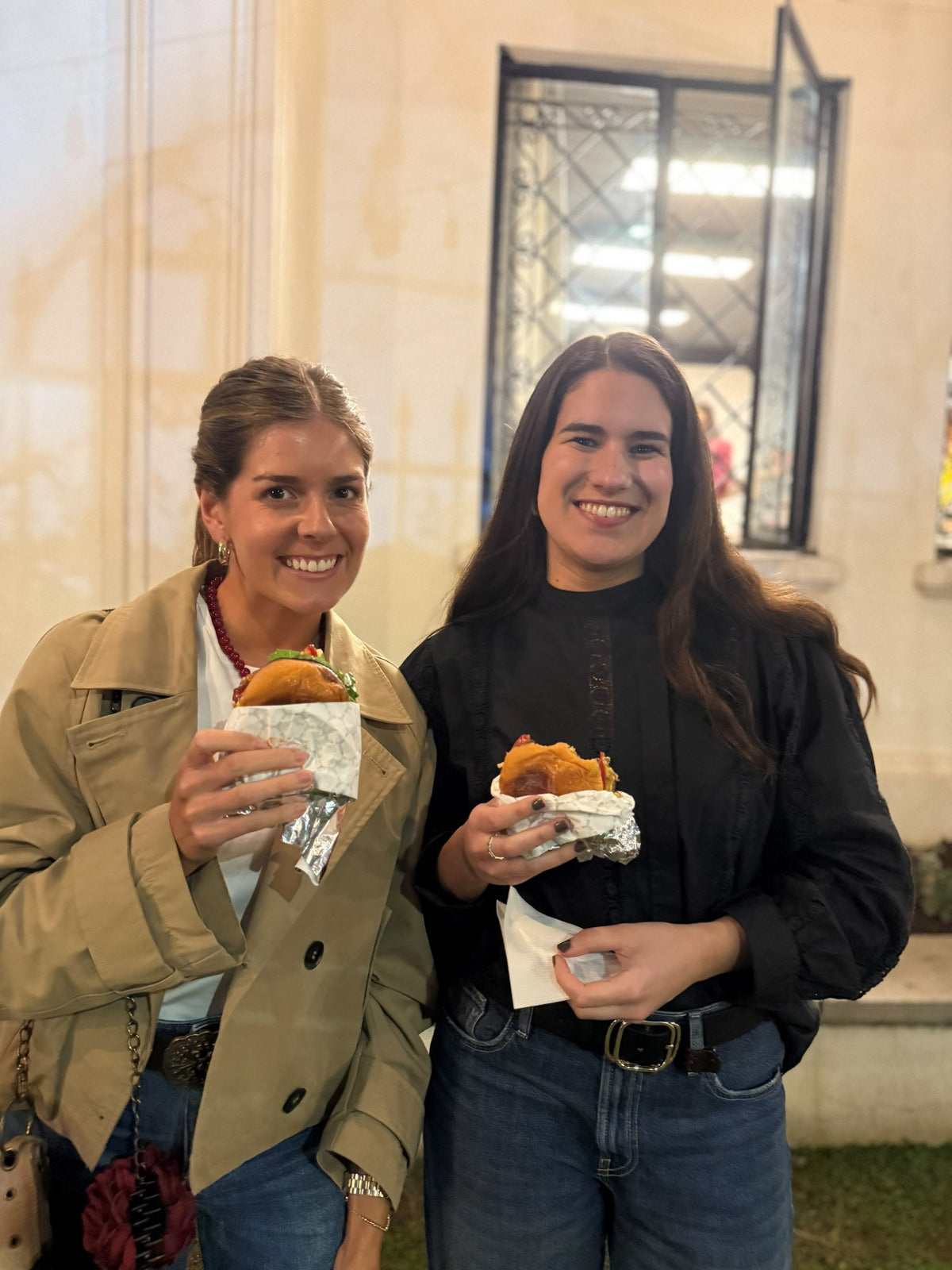 Dos invitadas disfrutando smash burgers en un evento de noche